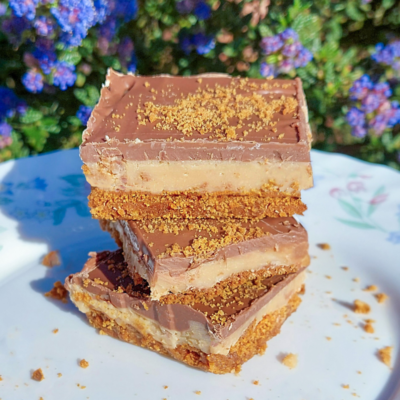 Stacked slices of millionaire’s gingerbread with a spiced gingerbread base, fudge layer and smooth chocolate topping on a plate outdoors.