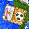 Football‑shaped iced gingerbread biscuit and Billington’s gingerbread presented in a gift box, styled with blue football boots and kit on artificial grass.