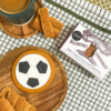 Football‑shaped iced gingerbread biscuit on a wooden board, styled with Billington’s gingerbread, loose gingerbread biscuits, and a mug on a checked kitchen cloth.