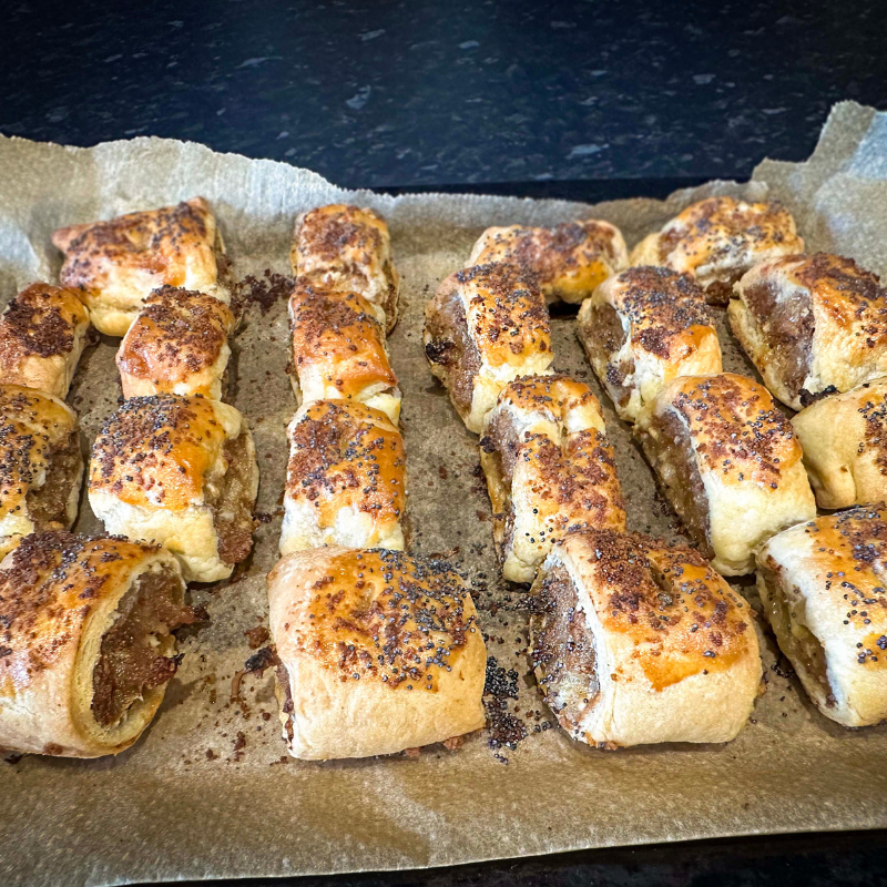 Freshly baked gingerbread sausage rolls with golden pastry and poppy seeds on lined tray