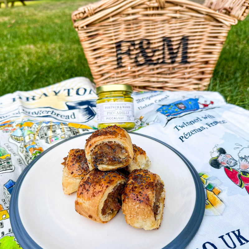 Close-up of gingerbread sausage rolls topped with poppy seeds, served on plate with picnic hamper and piccalilli