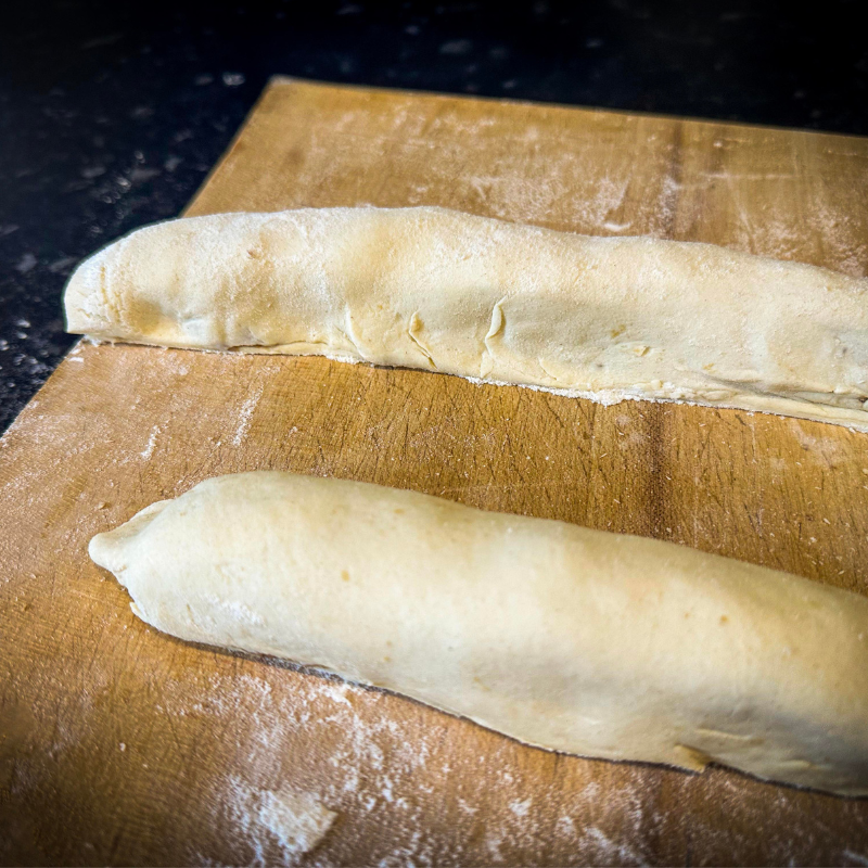 Unbaked sausage roll log wrapped in pastry on floured wooden board ready for cutting