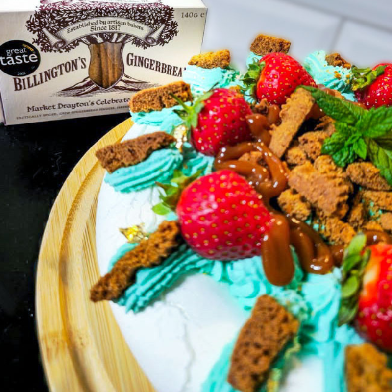 Billington's Gingerbread pavlova topped with fresh strawberries, whipped cream, crunchy gingerbread pieces and fresh mint, with a pack of Billington's Gingerbread in the background.