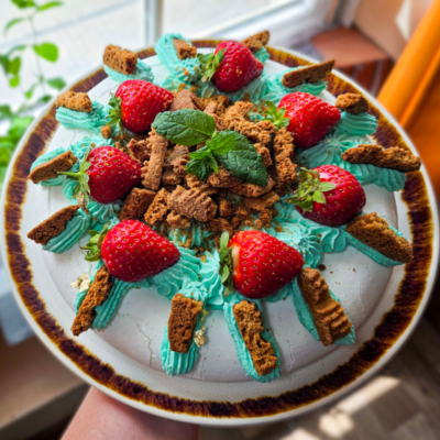 Billington's Gingerbread Pavlova topped with fresh strawberries, blue whipped cream, crunchy gingerbread biscuit pieces and mint leaves.